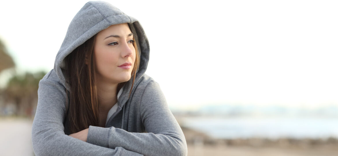 Portrait of a longing pensive teenager sitting on the beach looking away at the horizon in the morning_1600